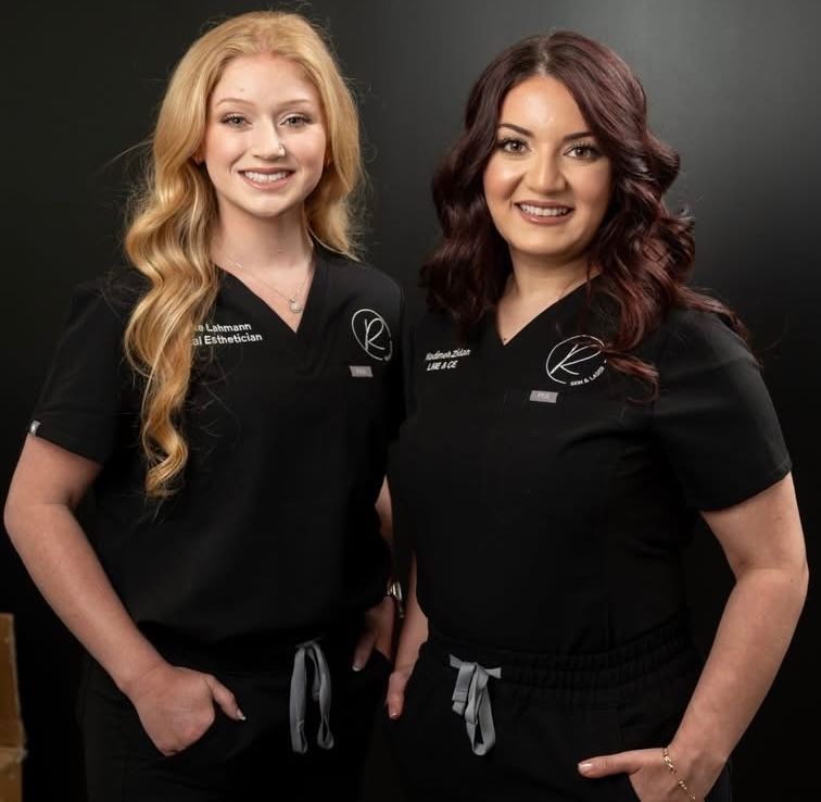 Two women in black uniforms standing side by side, smiling against a dark background