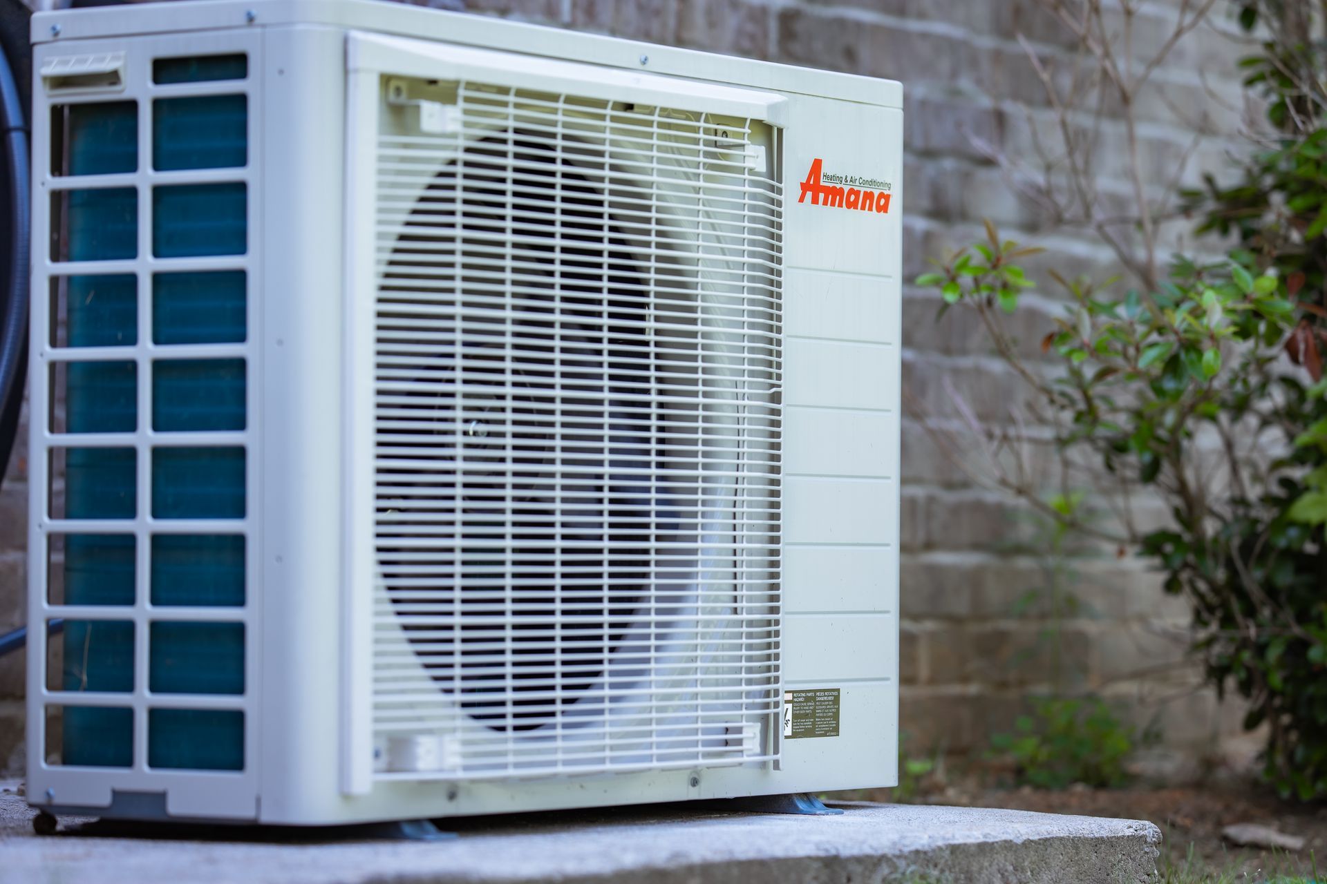 A white air conditioner is sitting on a concrete ledge next to a brick wall.