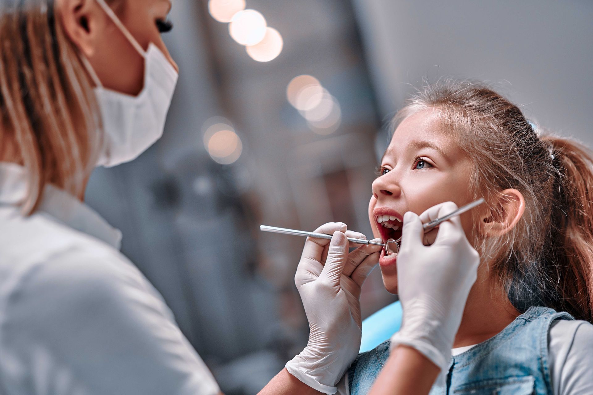 Un dentista esamina i denti di un bambino sorridente con uno specchietto e una sonda in una clinica.