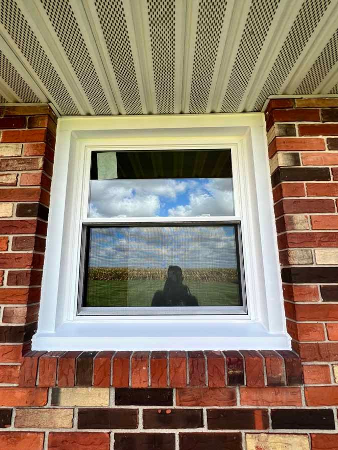 A white window on a brick wall with a reflection of a person in the window.