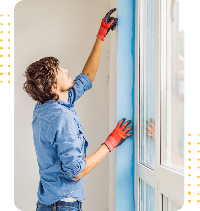 A man in a blue shirt and red gloves is painting a window.