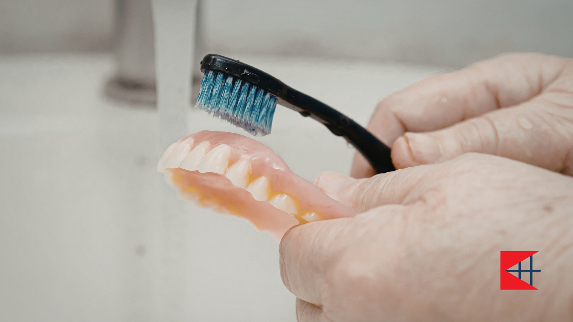 Person brushing dentures with a toothbrush over a sink.