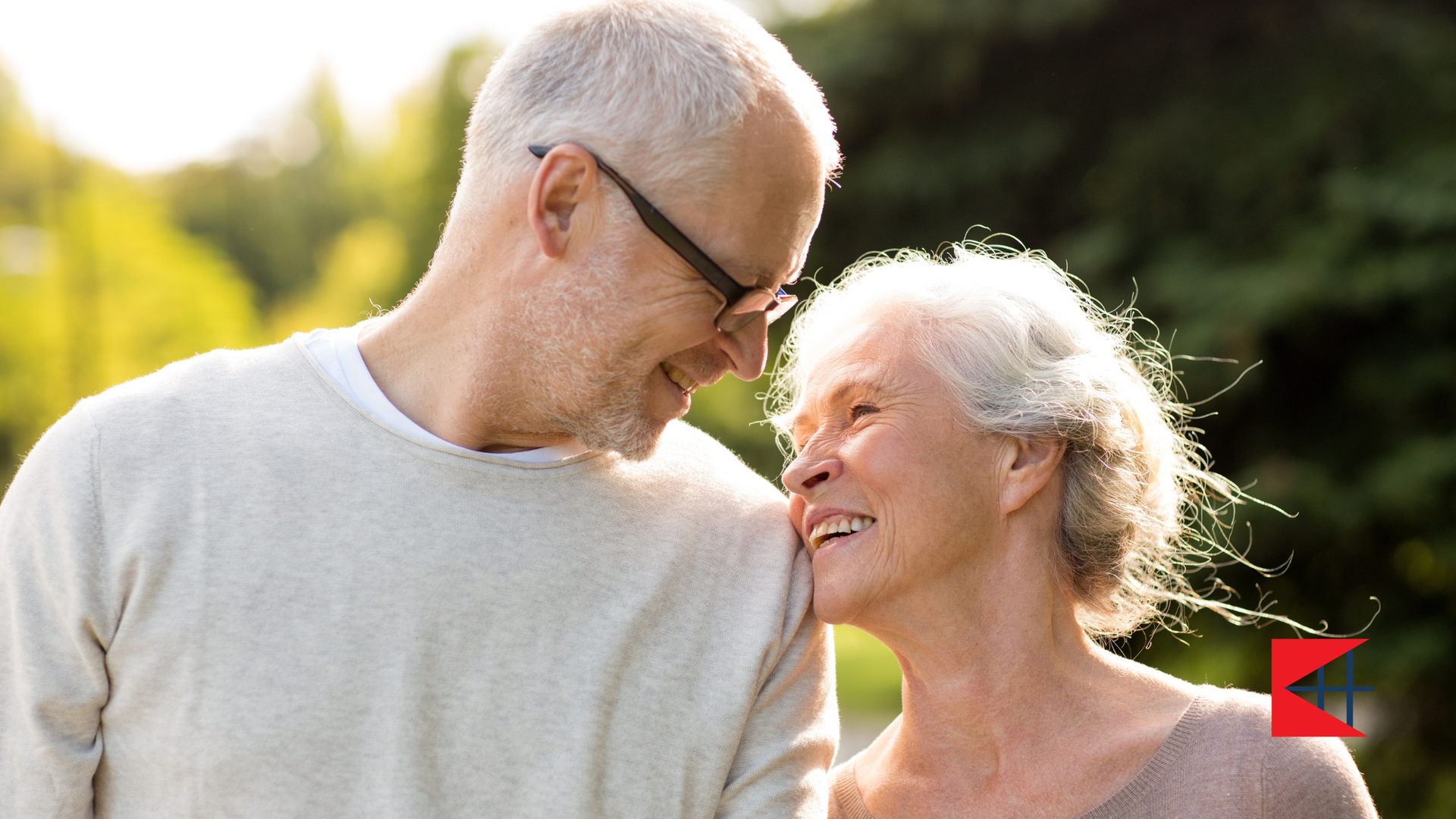 Smiling older couple looking at each other outdoors in sunlight.