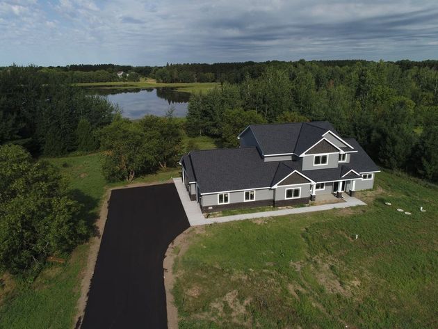 Aerial view of a gray house with a long driveway, surrounded by trees and a pond.