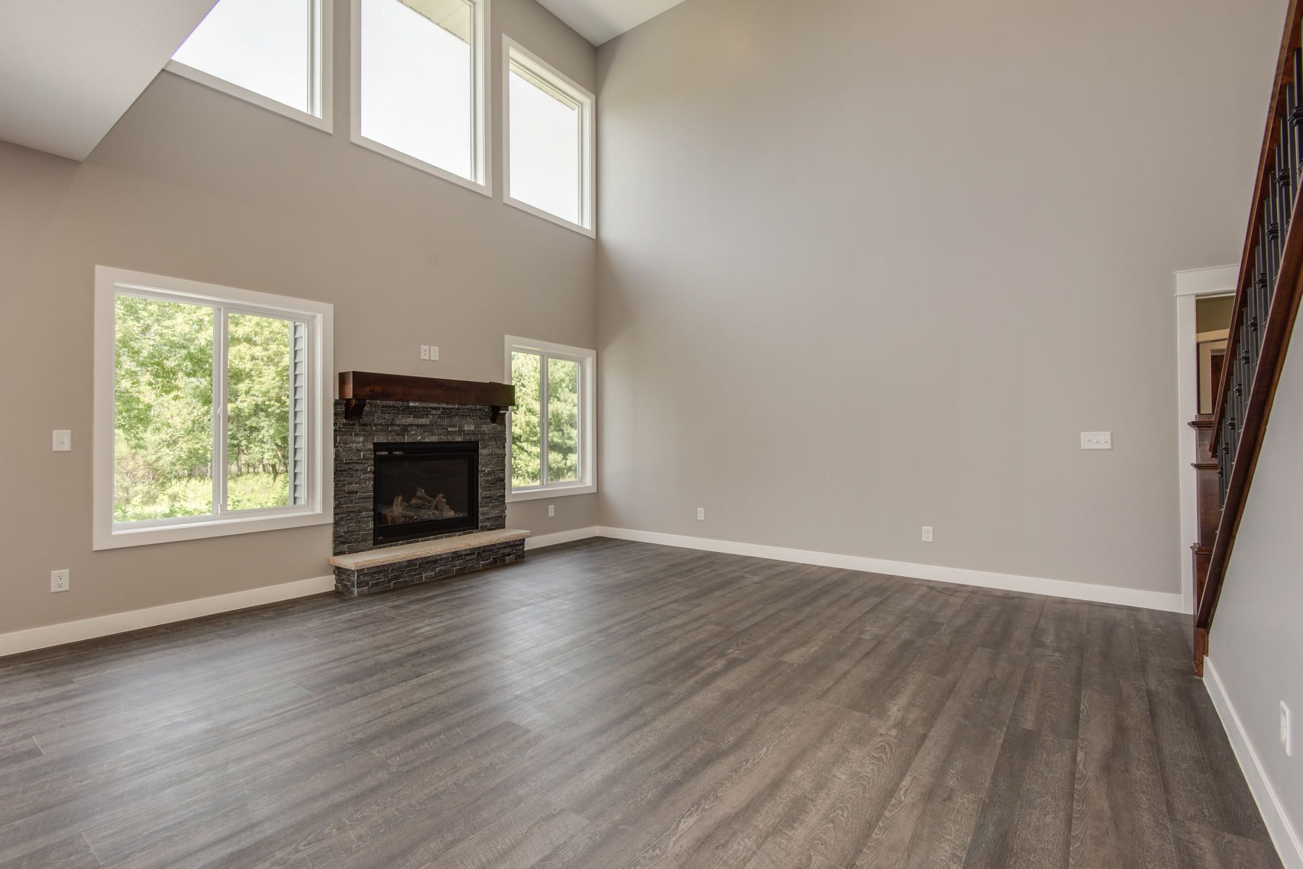 Spacious empty living room with gray floors, tall windows, and a corner fireplace