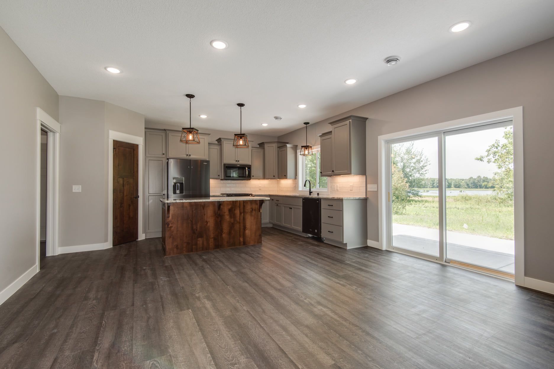 Open-concept kitchen and living area with dark wood floors, gray cabinets, and sliding glass doors to outside