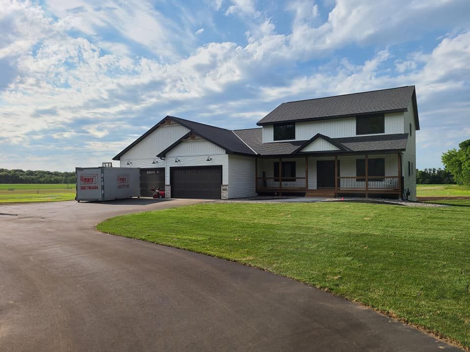 Modern two-story house with attached garage, curved driveway, and large green lawn under a cloudy sky