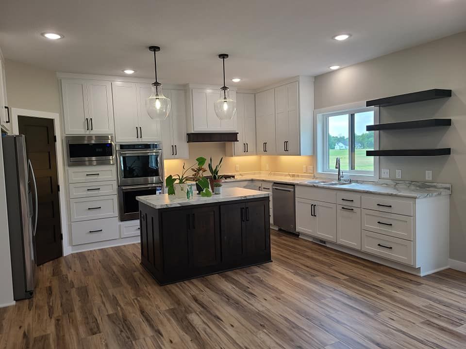 Modern kitchen with white cabinets, dark island, wood floors, and black pendant lights.