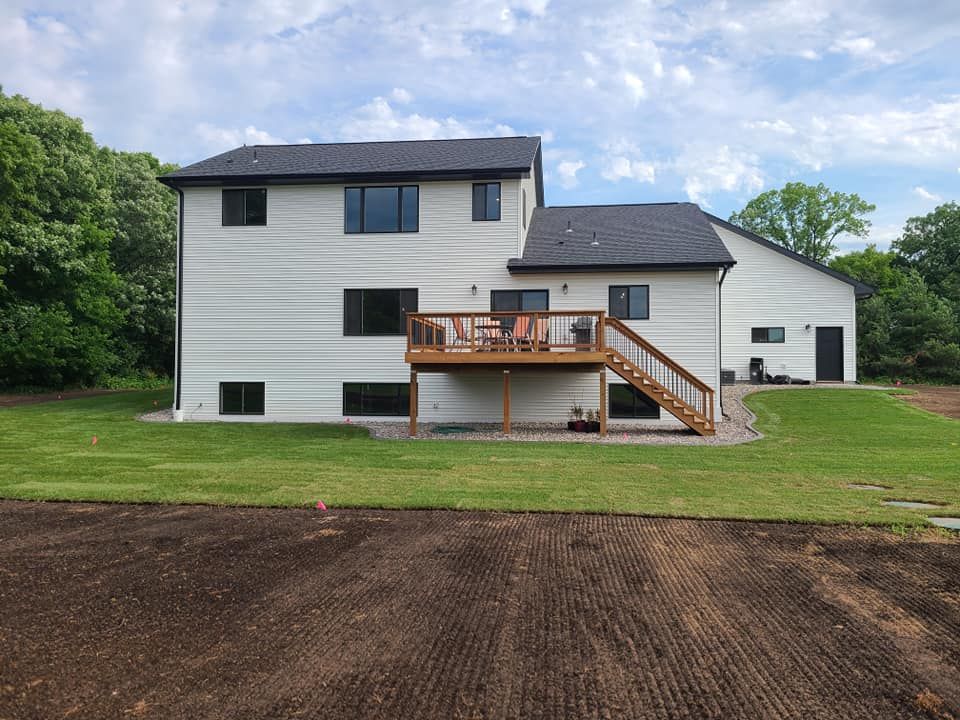 White two-story house with a deck and stairs, set behind a large dirt yard and green lawn