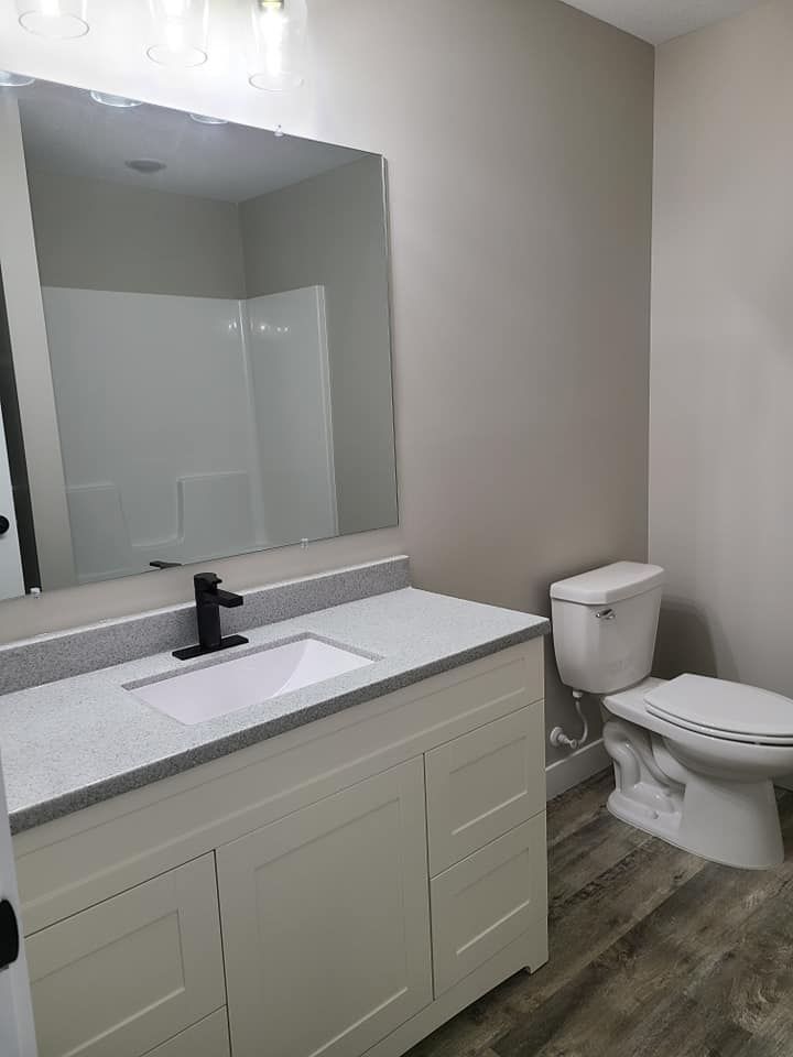 Modern bathroom vanity with mirror, white sink and toilet, gray walls, and wood-look flooring