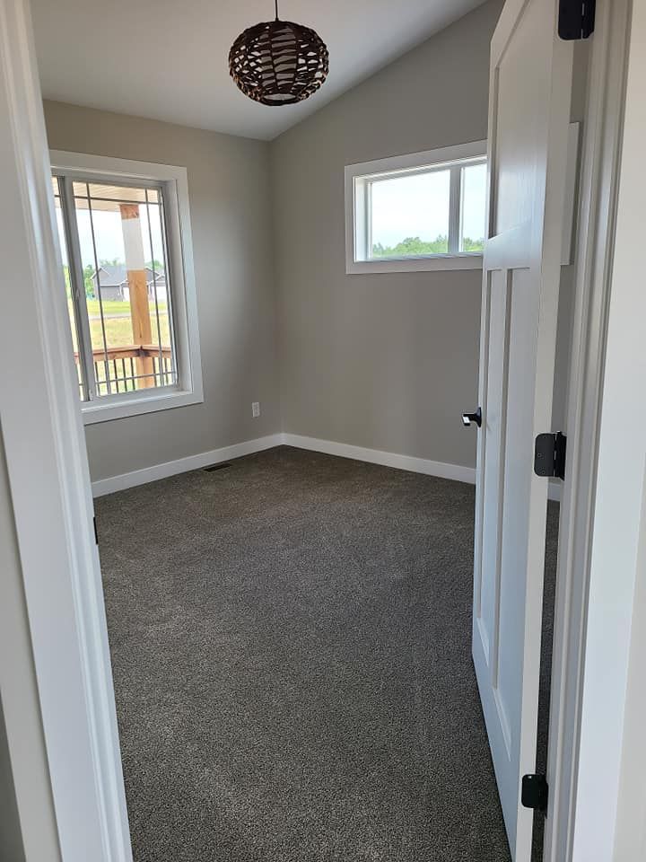 Empty gray-carpeted room with white walls, two windows, and a hanging light fixture