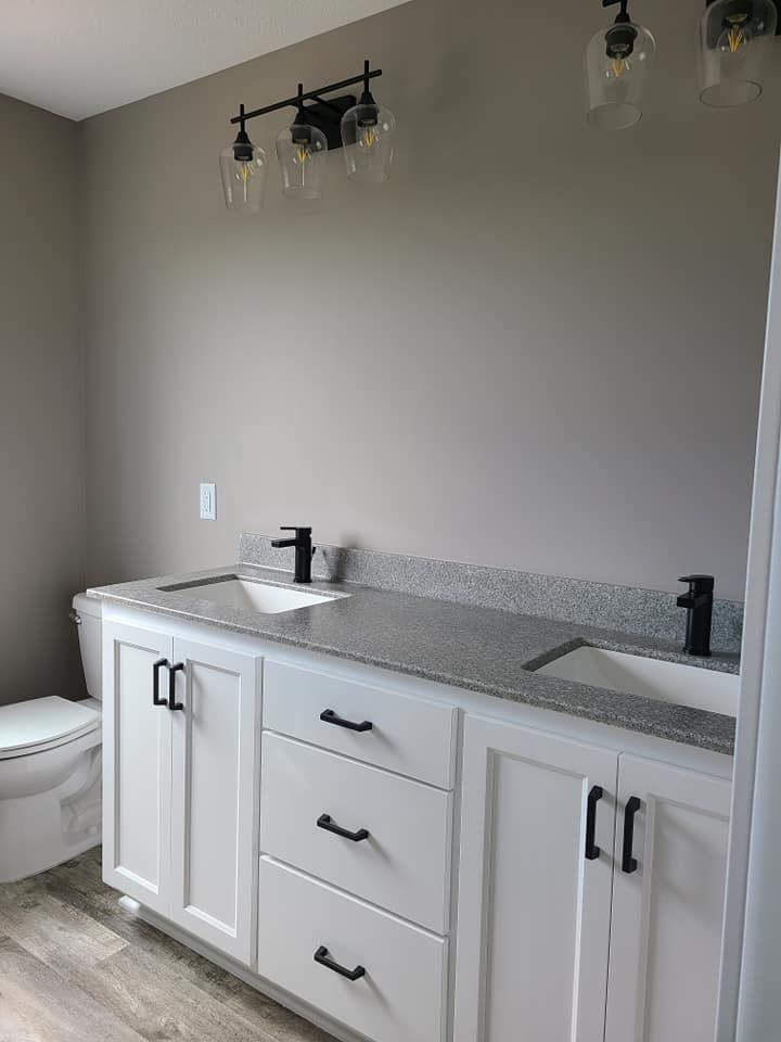 Bathroom vanity with white cabinets, gray countertop, sink, and wall-mounted light fixture.