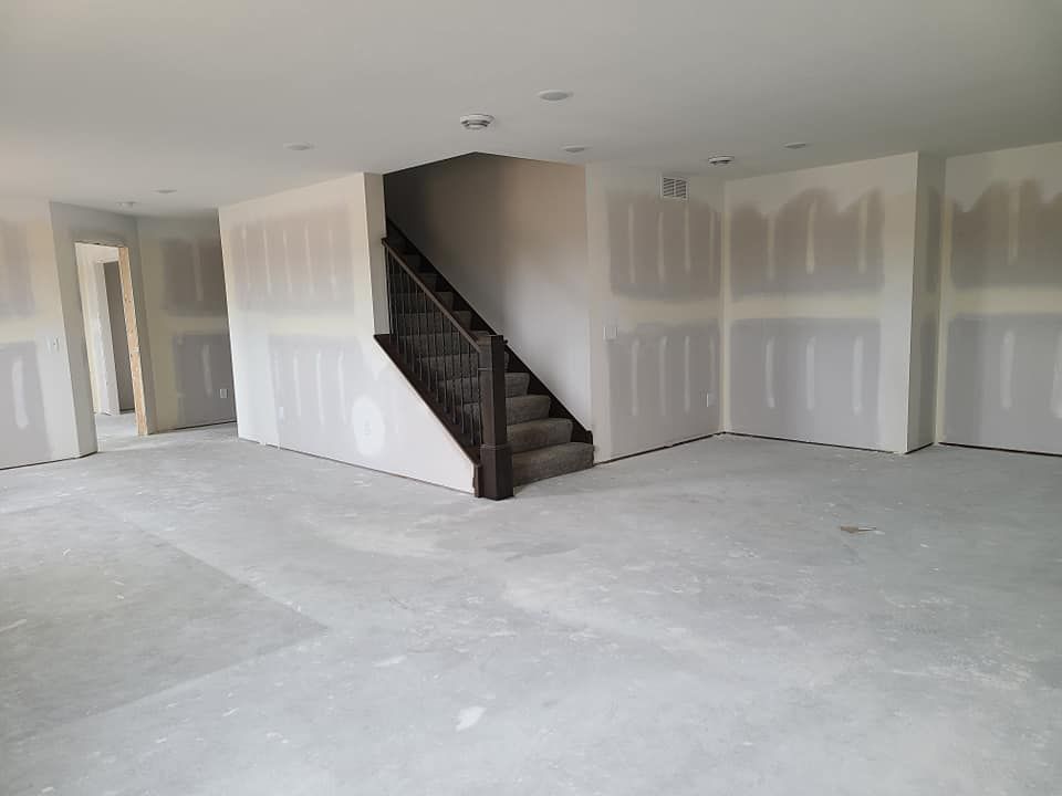 Empty unfinished room with drywall, gray carpet, and a staircase in the center