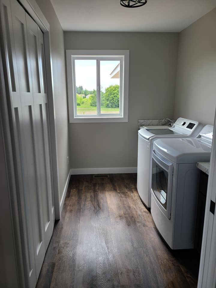 Laundry room with washer and dryer, gray walls, dark wood floor, and a window overlooking trees