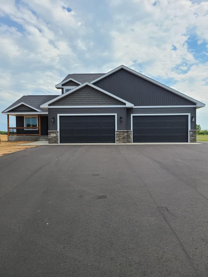 Modern gray suburban house with three-car garage and wide driveway under a cloudy sky