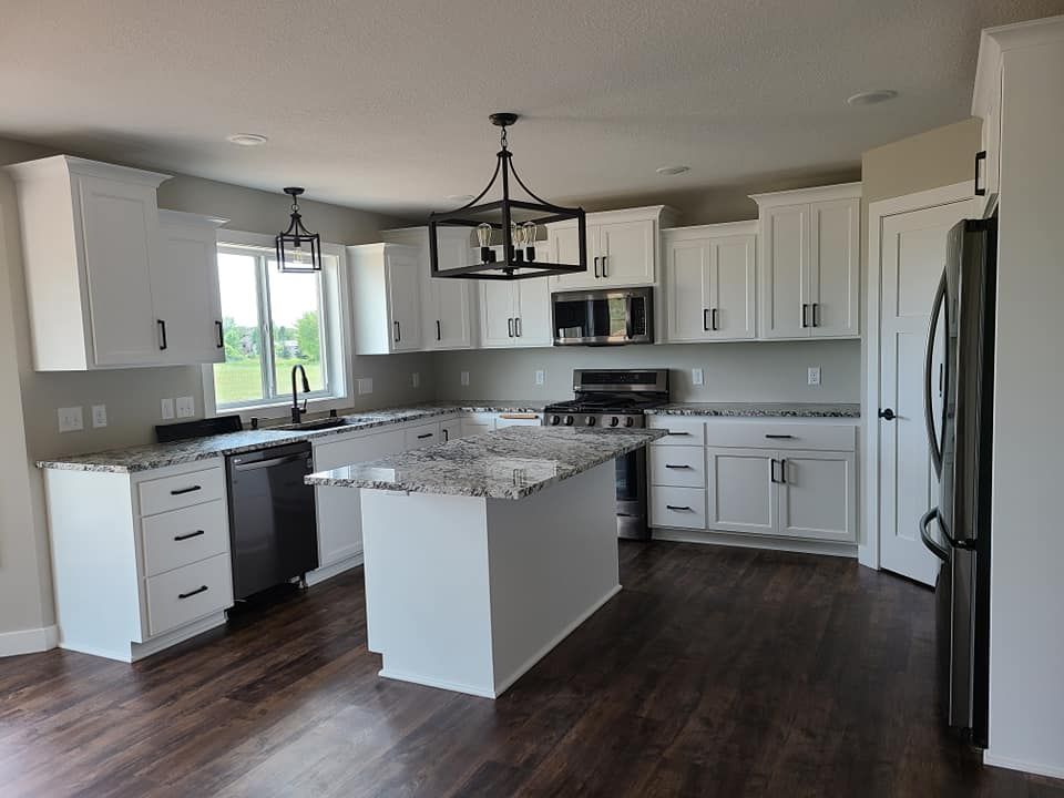 Bright modern kitchen with white cabinets, dark floors, island, granite countertops, and black chandelier