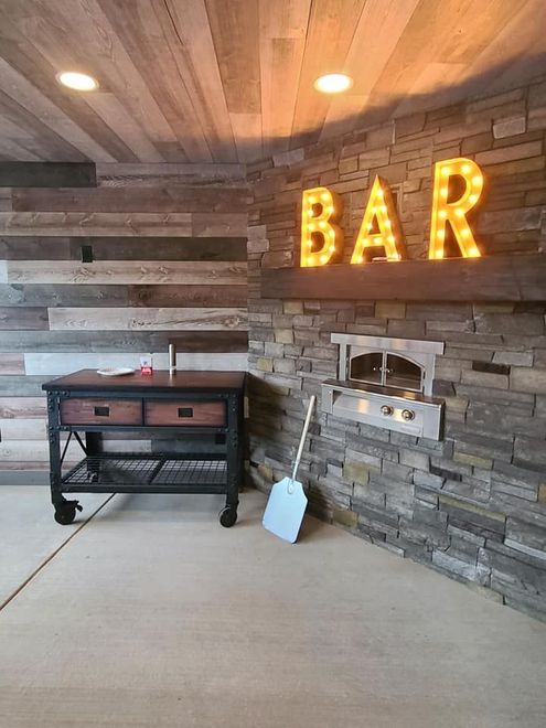 Rustic bar area with stone wall, wooden ceiling, lit “BAR” sign, and a grill on the patio.