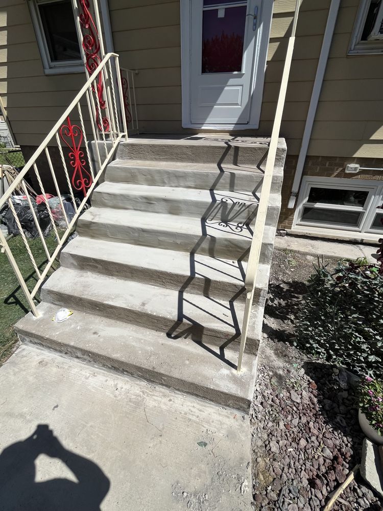 Front steps to a house with white railings, a concrete walkway, and a black metal handrail on the right.