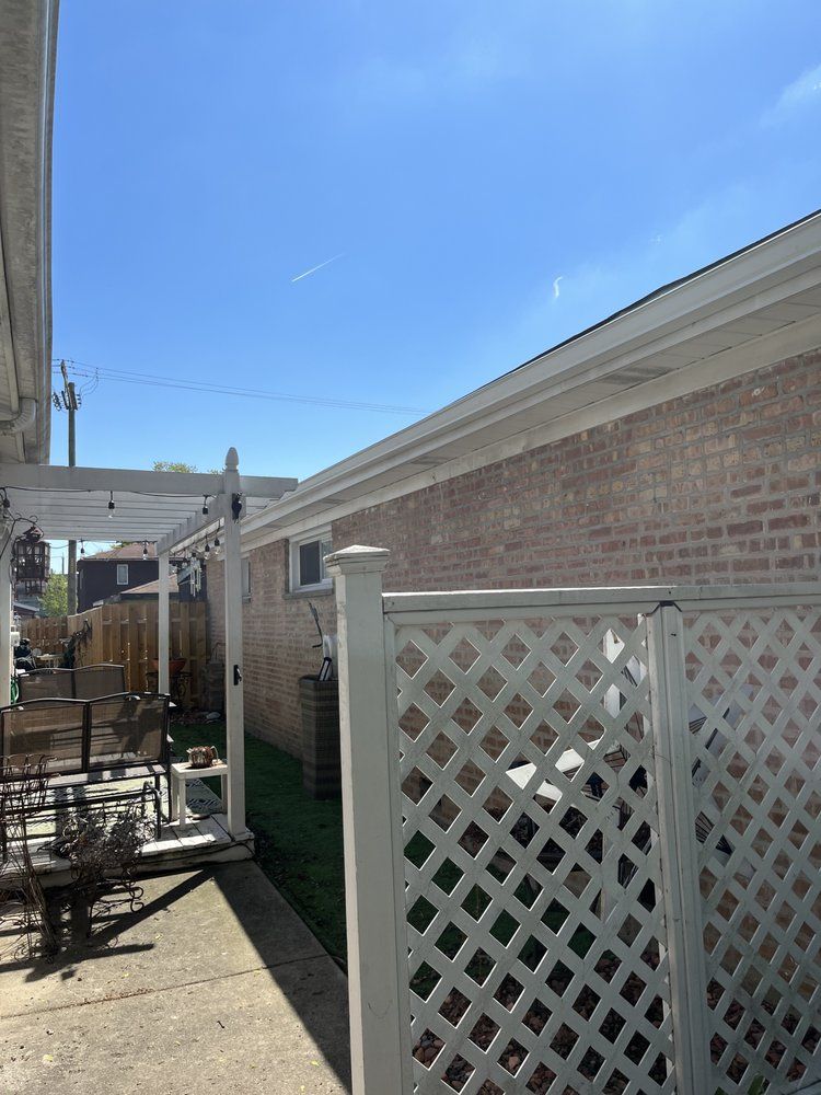 Backyard patio with white lattice fence, brick house, and blue sky on a sunny day