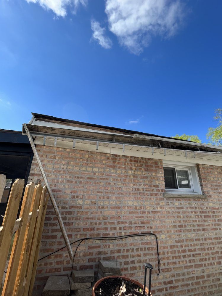 Brick house exterior with leaning ladder, wooden fence, and blue sky with clouds