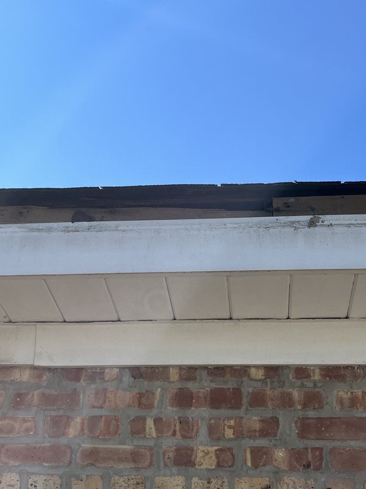 Brick wall beneath white eaves and roof edge against a clear blue sky