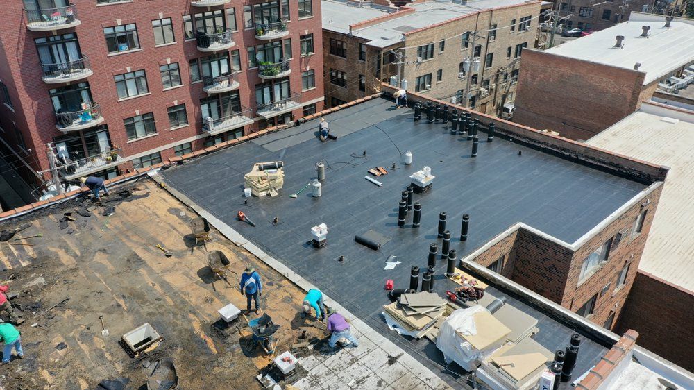 Rooftop under construction with workers and a black waterproof surface on a city building.