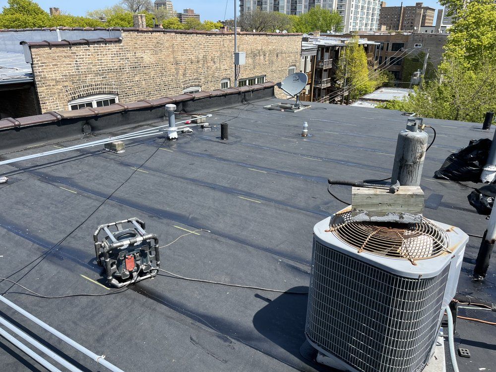 Flat rooftop with HVAC units, vents, and cables beside a brick parapet under a clear sky.