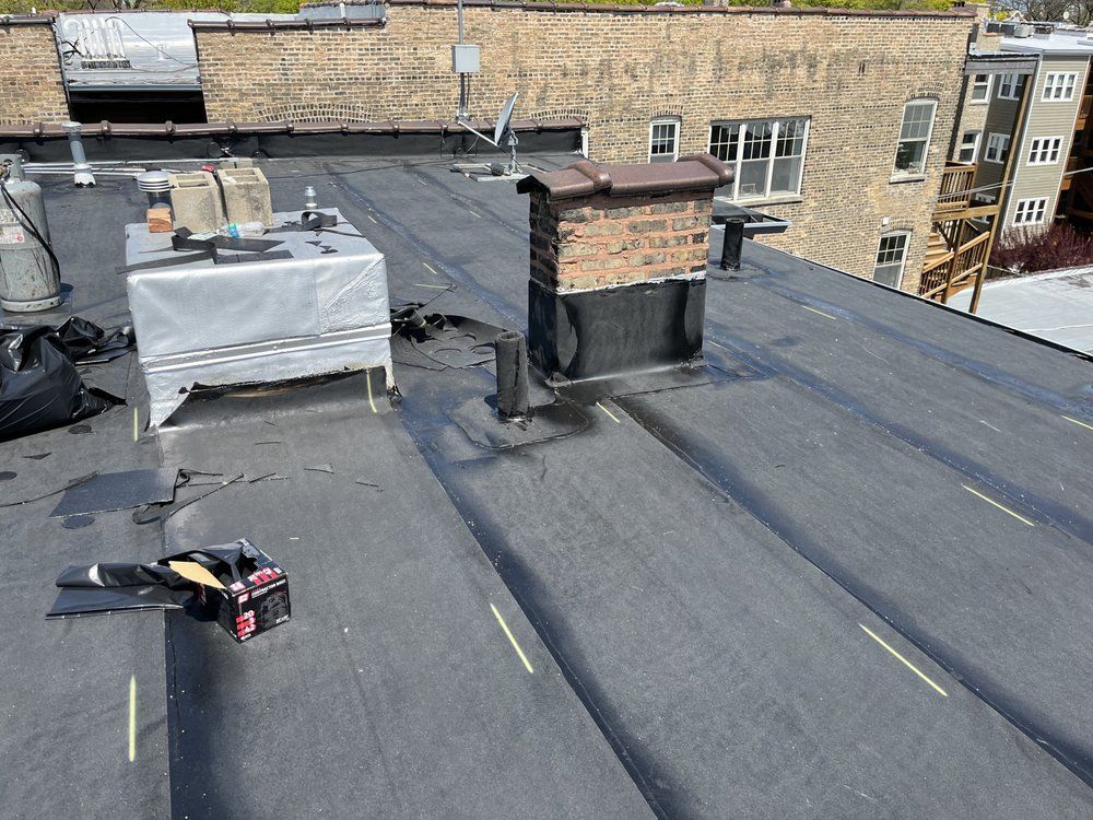 Rooftop with black waterproofing, vents, HVAC units, and nearby brick buildings in the background