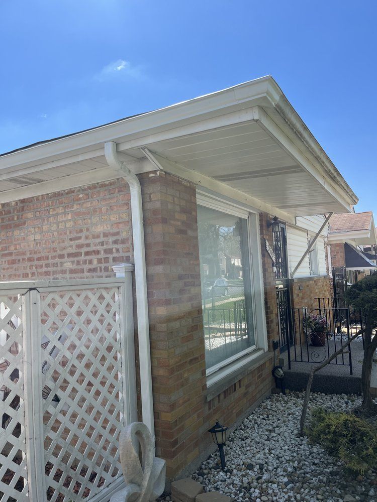 Brick house corner with white lattice fence, large window, and gravel yard under blue sky