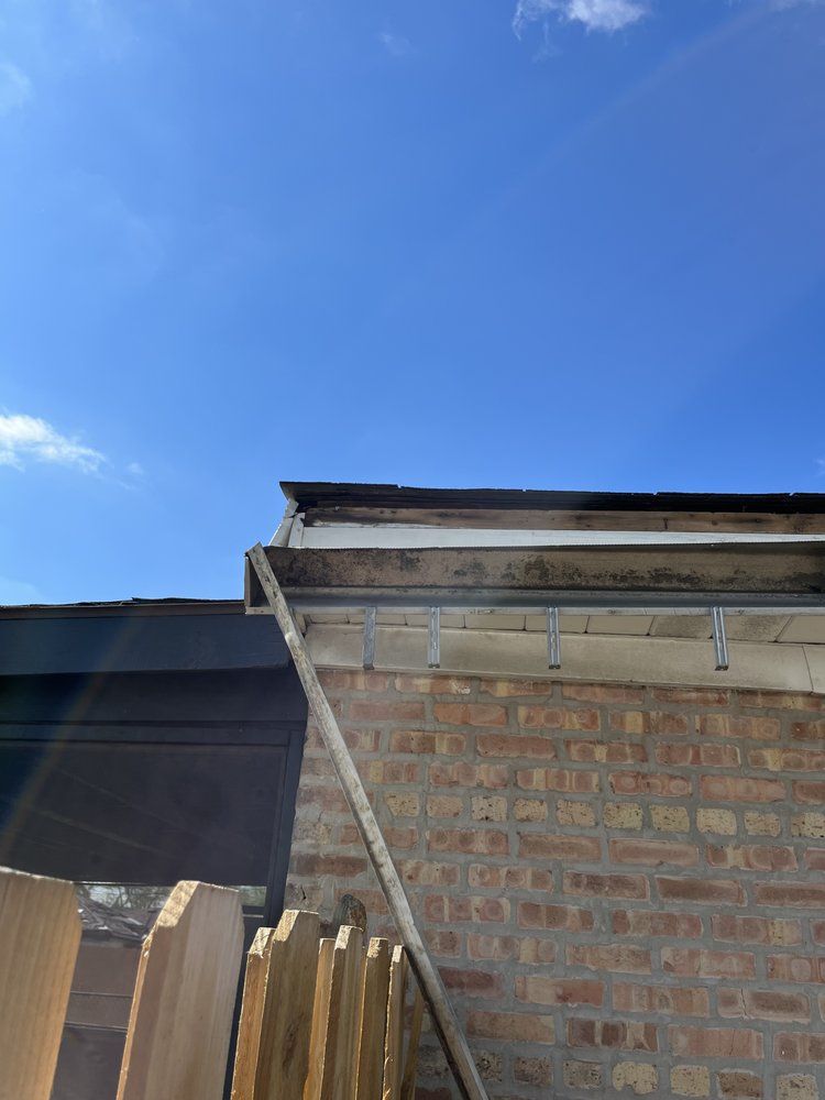 Brick house eave and roofline against a clear blue sky, with a wooden fence below.