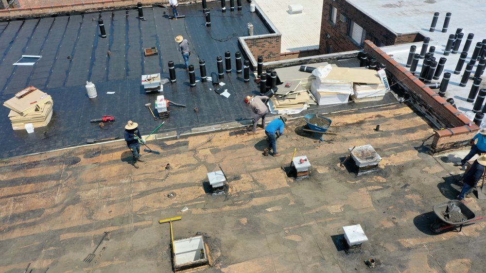 Roofing workers installing materials on a flat rooftop beside a brick building.