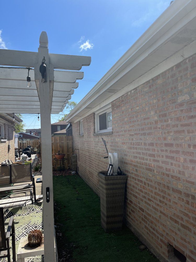 Narrow backyard walkway beside a brick house, with a white pergola post and green artificial turf.