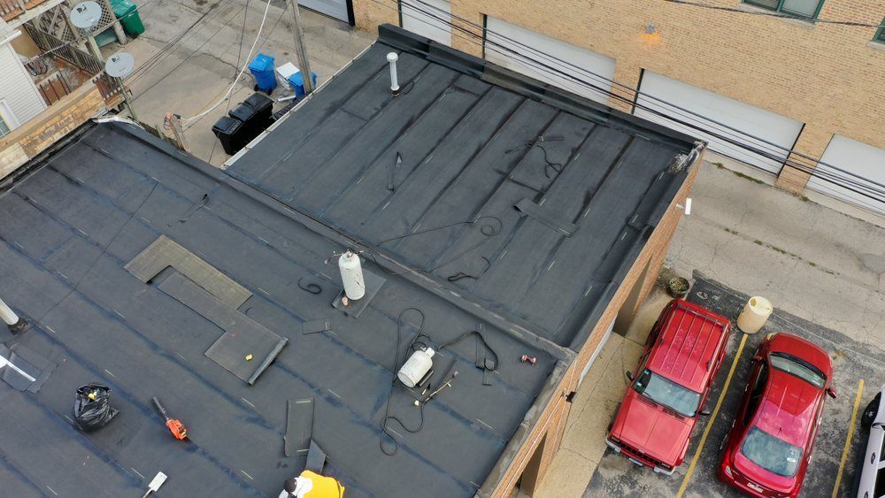 Aerial view of a black-roofed building beside a street and parking lot with two red cars.
