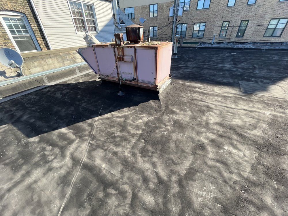 Rooftop with a pink HVAC unit on a dark membrane roof beside brick buildings