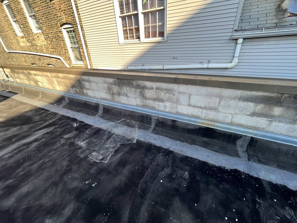Rooftop beside beige siding with visible water damage and black tar roofing under repair