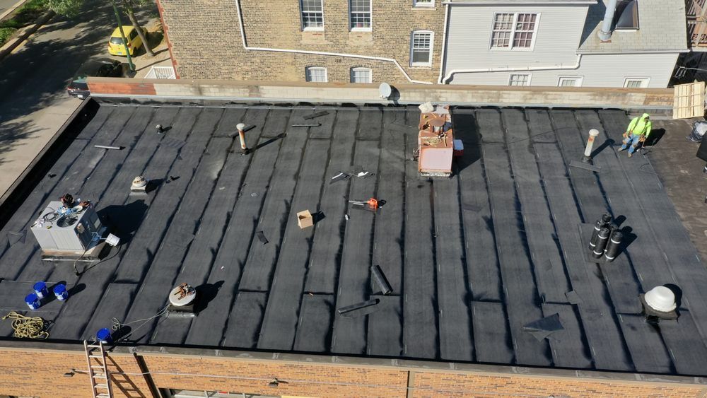 Workers installing black roofing on a flat rooftop with tools and materials scattered across it