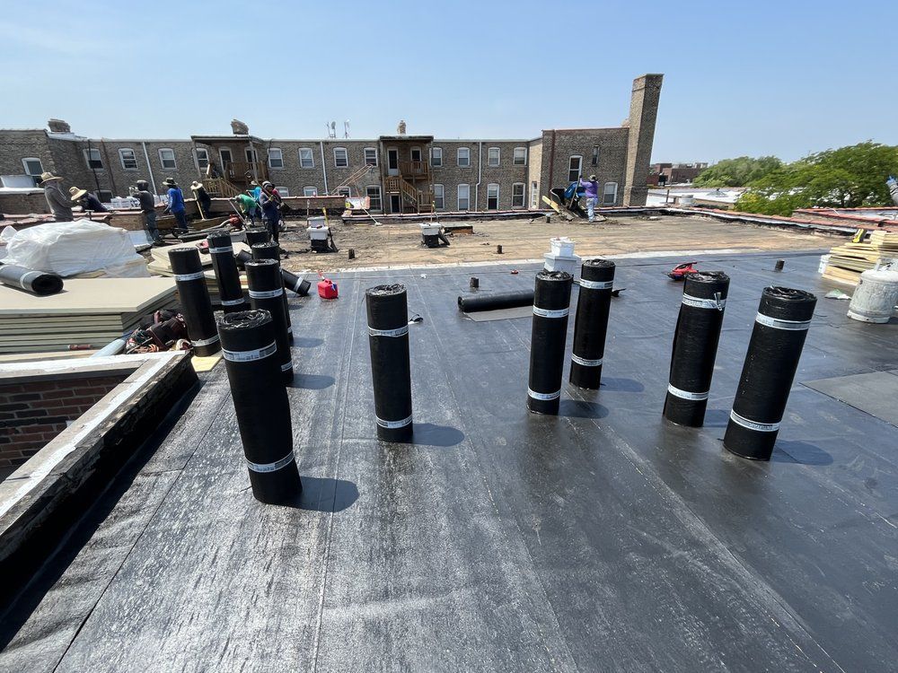 Rooftop under construction with black vents in foreground and a brick apartment building in the background