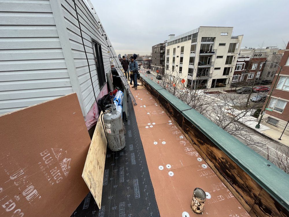 Workers on a rooftop walkway with tools and materials beside apartment buildings under construction.
