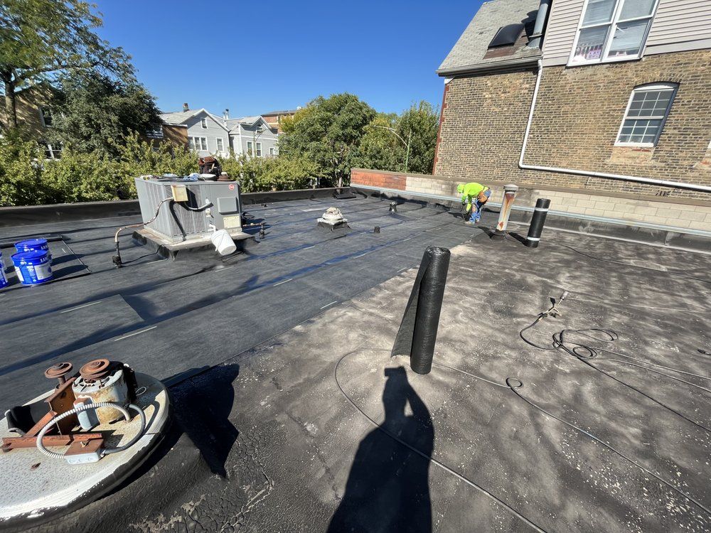 Workers installing black roofing on a flat-roof house under a clear blue sky