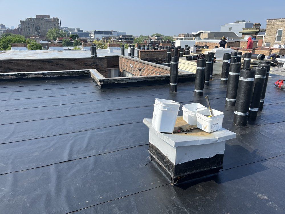 Flat rooftop with black waterproofing, white vent boxes, and several black vents against a city skyline
