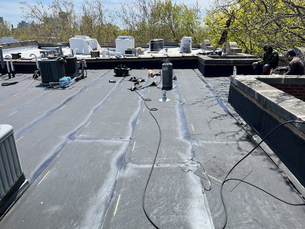Flat black rooftop with HVAC units, skylights, and workers near the far edge under trees.