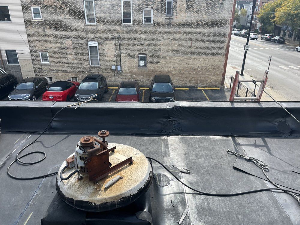 Rooftop view of a circular vent cap and cables beside parked cars and a brick building.