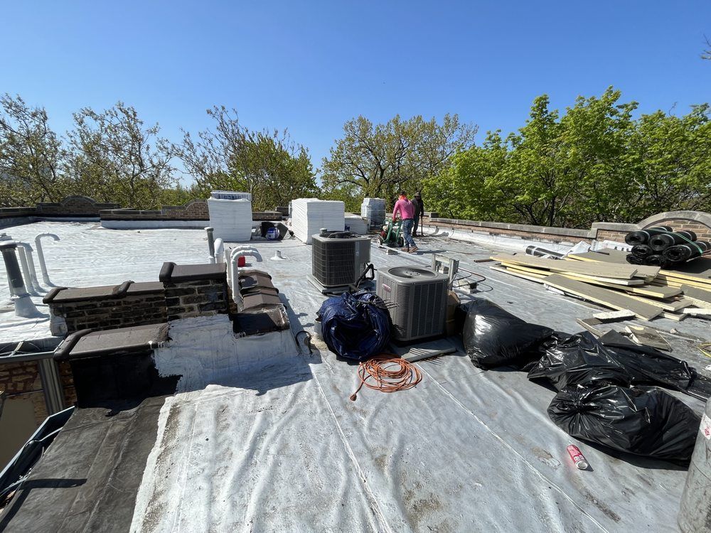 Rooftop with HVAC units, tools, and materials spread across a white membrane under a clear blue sky