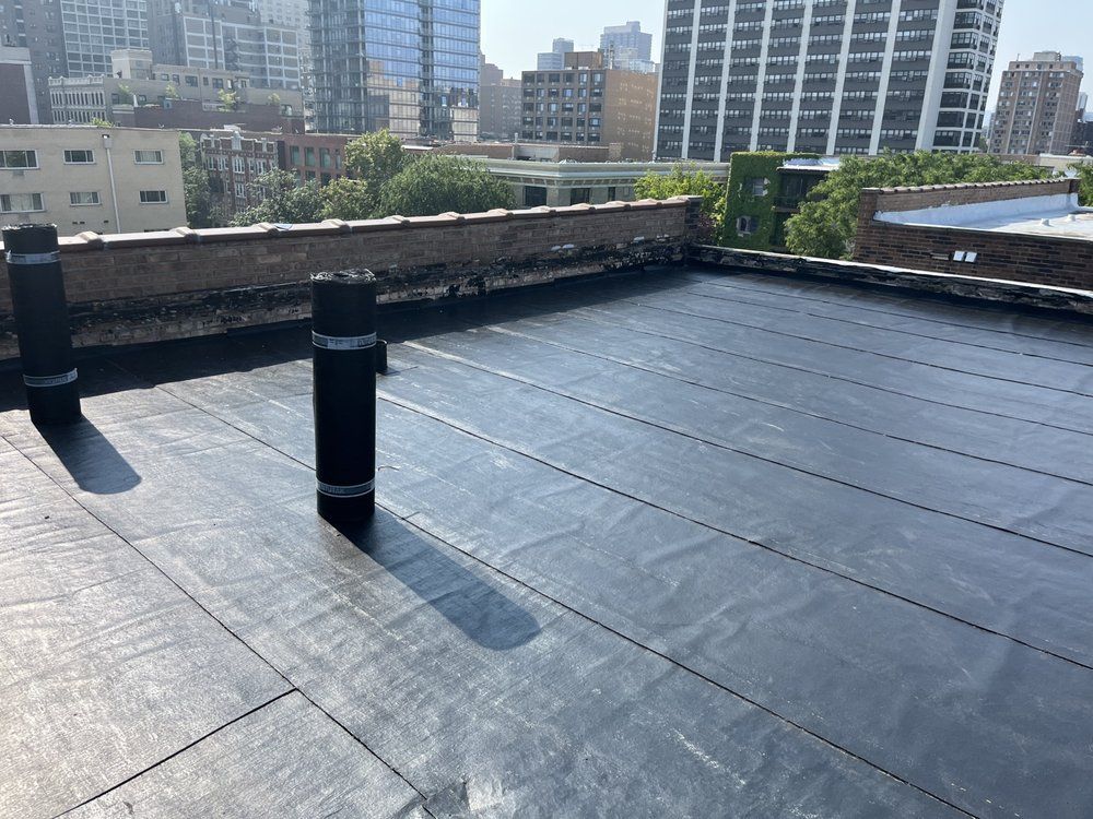 Flat rooftop with black roof vents, city buildings in the background.