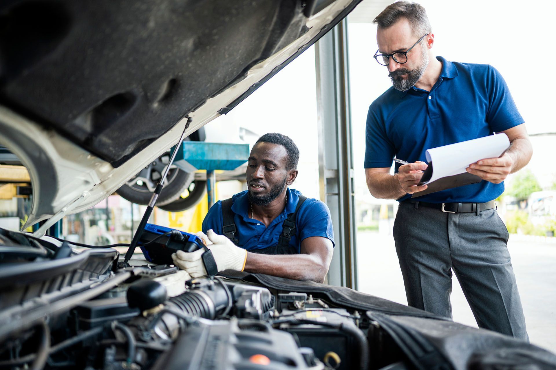 A technician is next to a man investigating a car engine breakdown.
