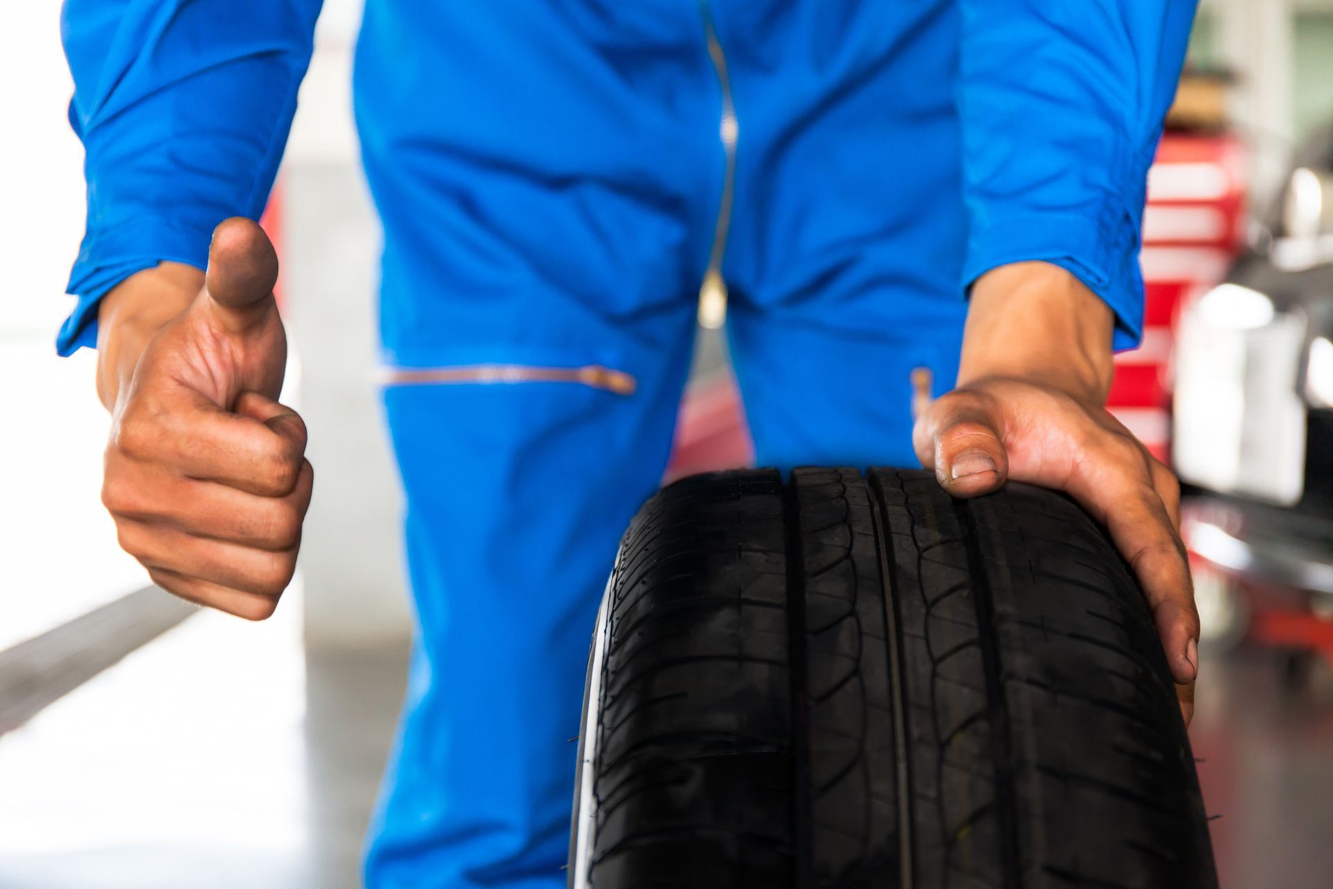 Mechanic in blue uniform inspecting a tire with a thumbs-up at a tire shop in Chula Vista, CA.