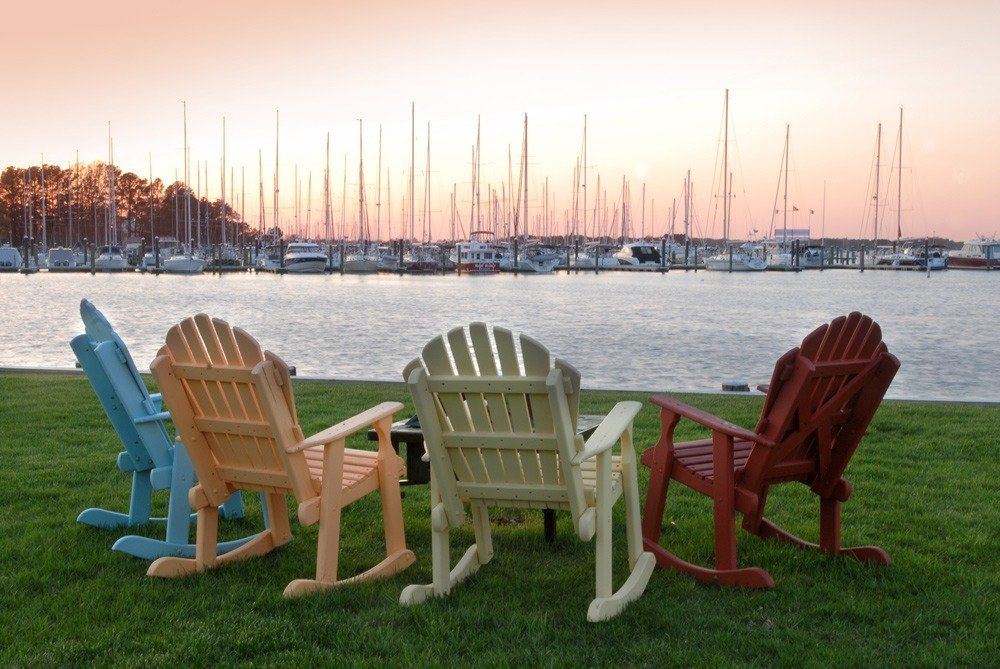 Rocking chairs on a grassy lawn with water, marina and boats in the background