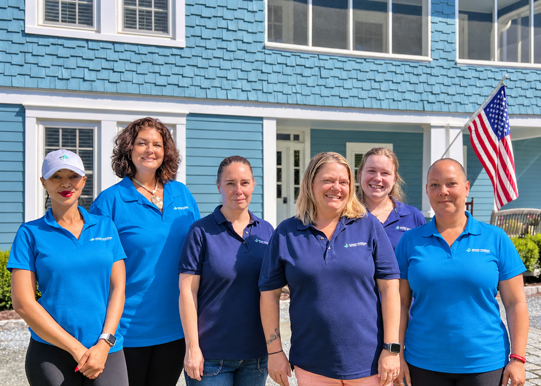 Six people in blue shirts standing outside a blue building, with an American flag visible