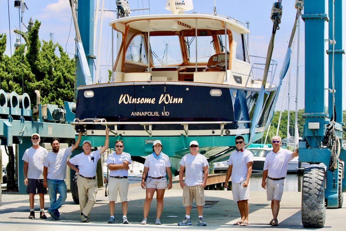 Employees stand with freshly painted boat in a lift before it leaves the boatyard