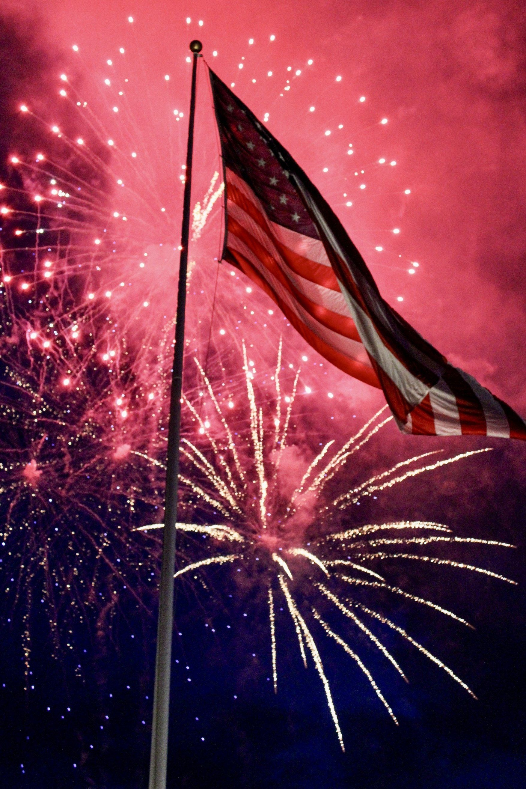 Fireworks at night behind a flying American flag